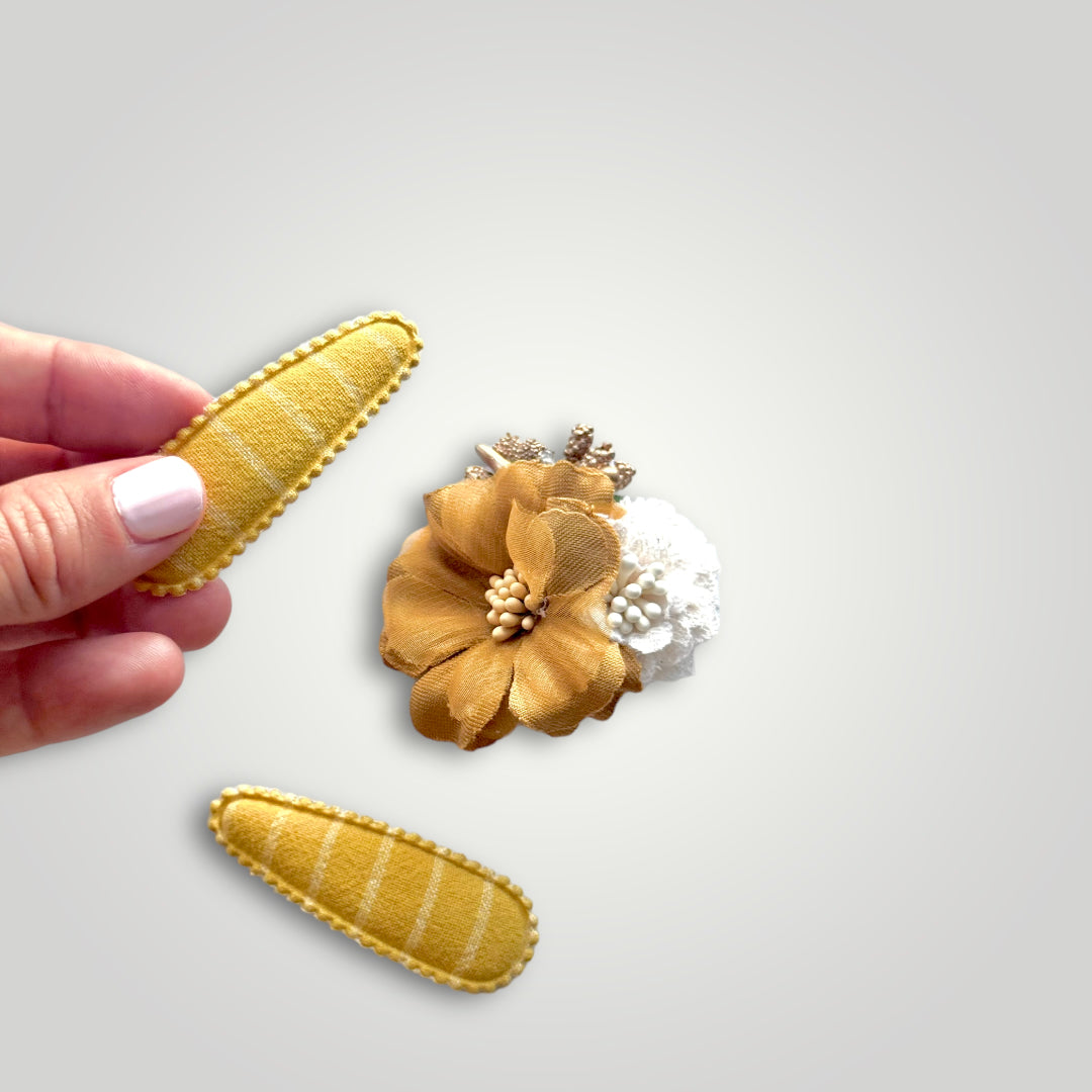 Set of 3 clips; 1 snap clip with a golden hues and a white flower and 2 snap clips covered with mustard colored fabric.