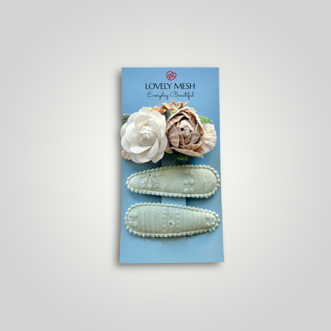 Set of 3 clips; 1 snap clip with a taupe and a white flower, and 2 snap clips covered by aqua embroidered fabric.