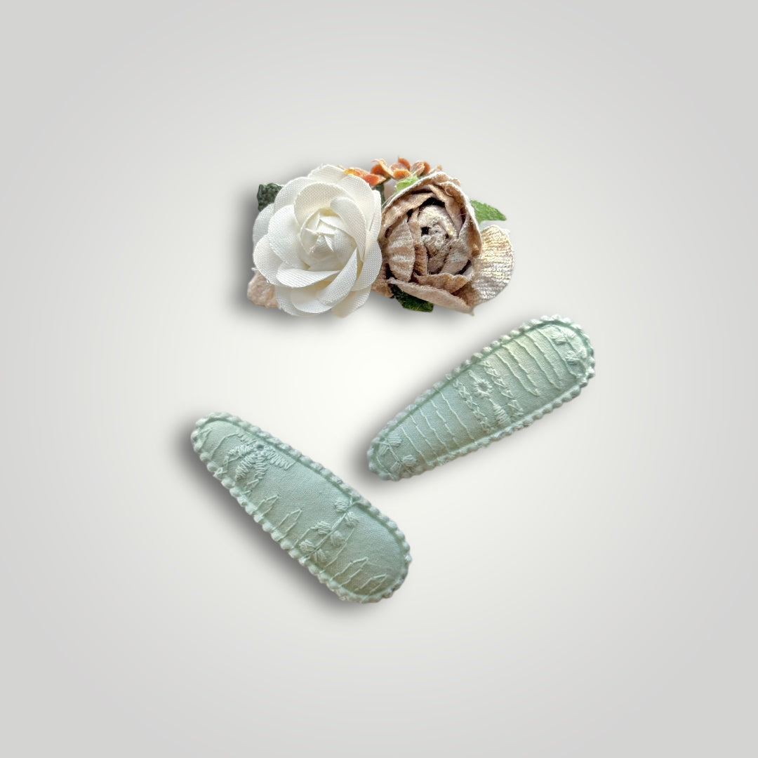 Set of 3 clips; 1 snap clip with a taupe and a white flower, and 2 snap clips covered by aqua embroidered fabric.