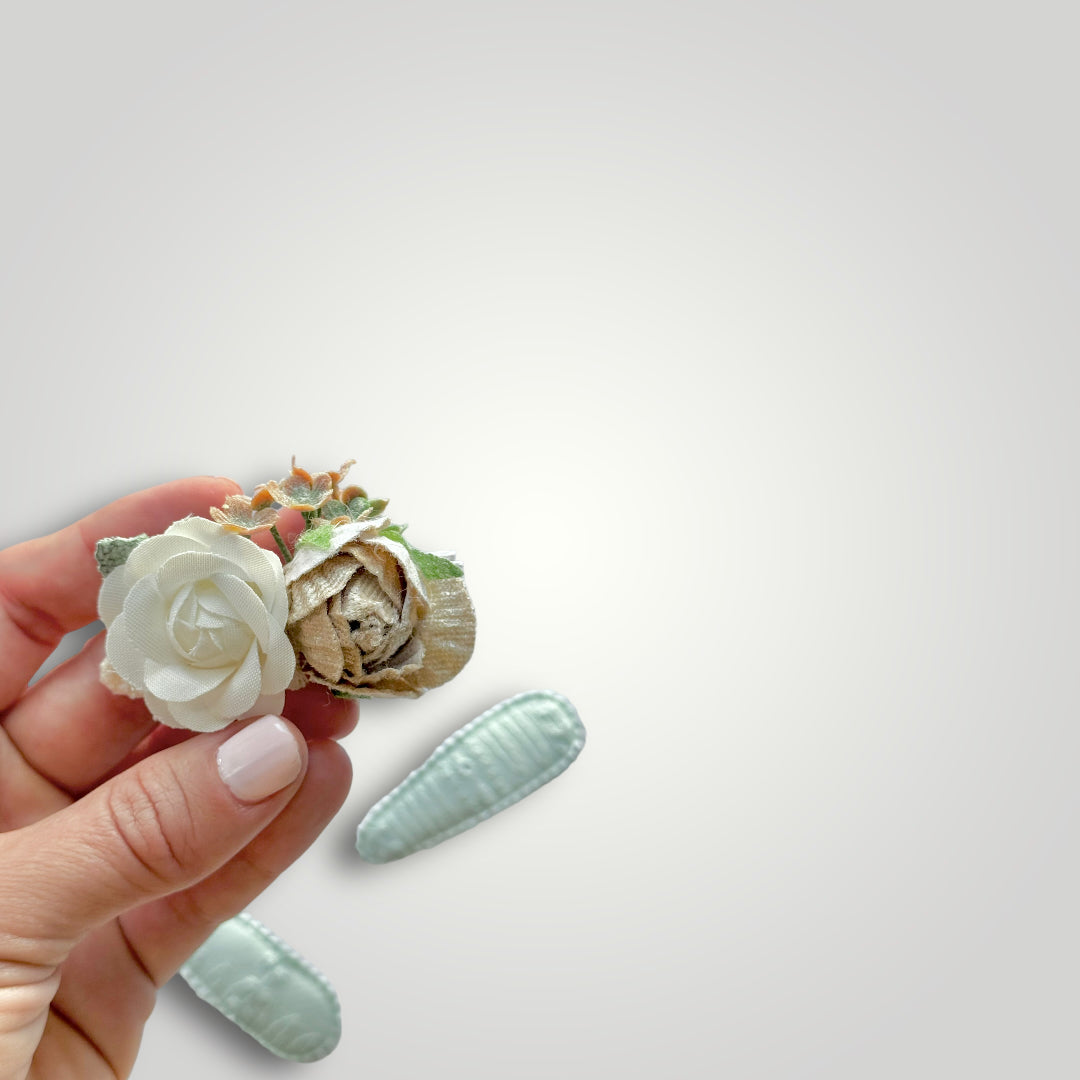 Set of 3 clips; 1 snap clip with a taupe and a white flower, and 2 snap clips covered by aqua embroidered fabric.