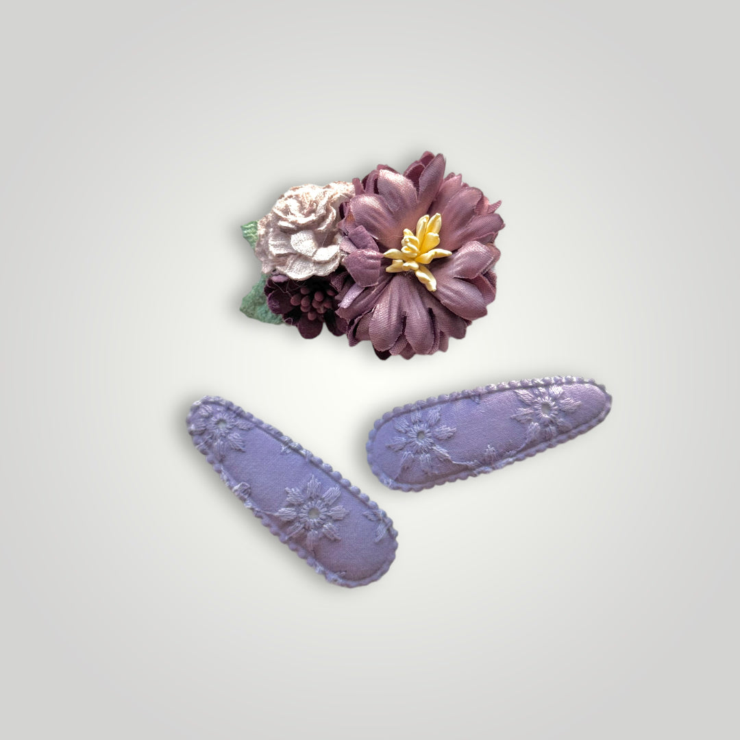 Set of 3 clips; 1 snap clip with purple and lila flowers and 2 snap clips covered with embroidered purple fabric.