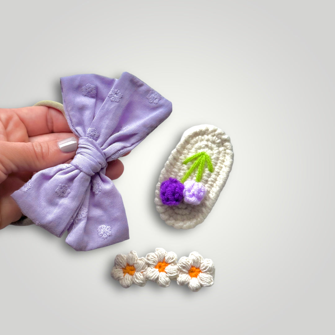 1 embroidered gauze bow in a soft headband with 2 crocheted clips, one with flowers and one with fruits. Colors: Purple, lila, off white and orange.