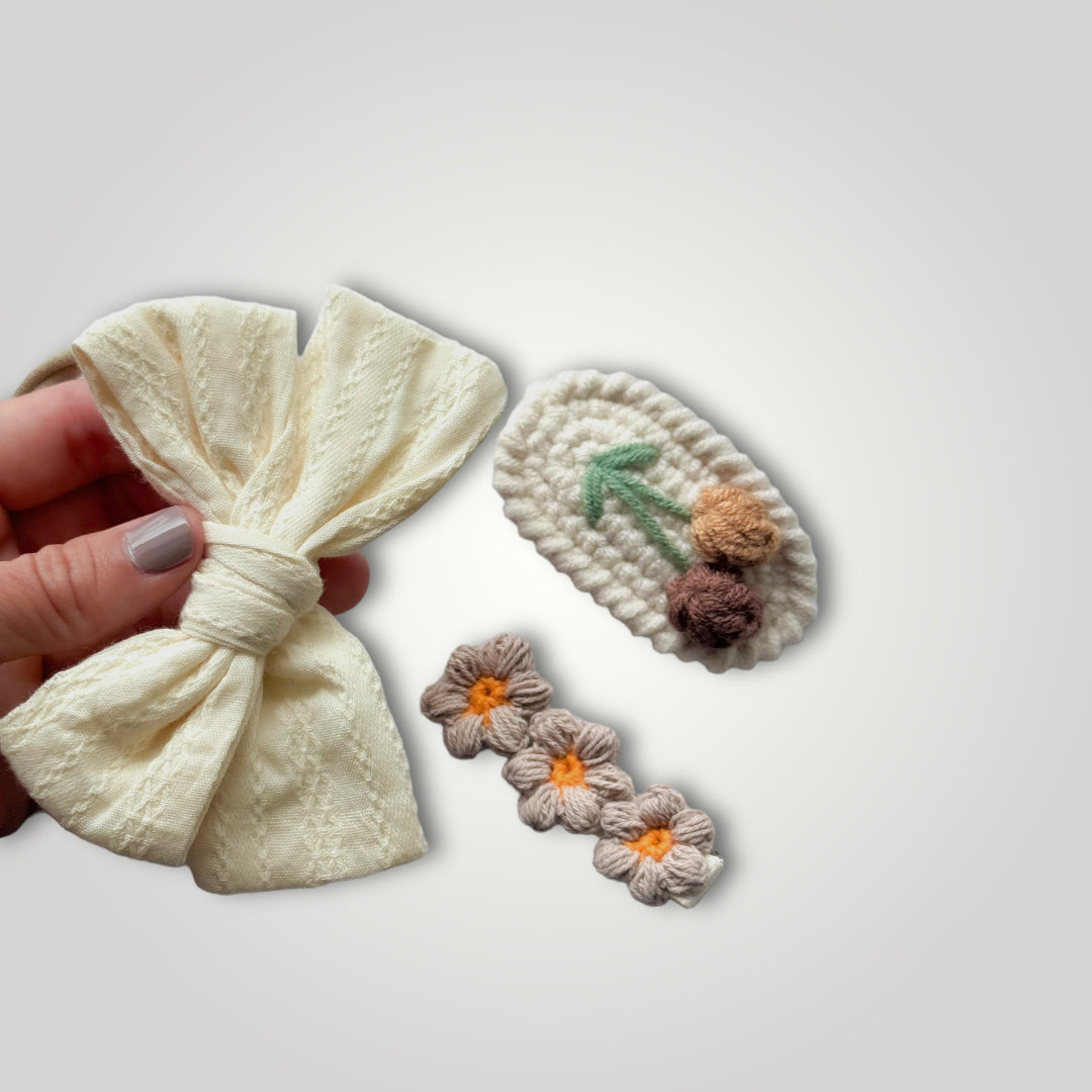 1 embroidered gauze bow in a soft headband with 2 crocheted clips, one with flowers and one with fruits. Colors: Off white, brown, green and orange.