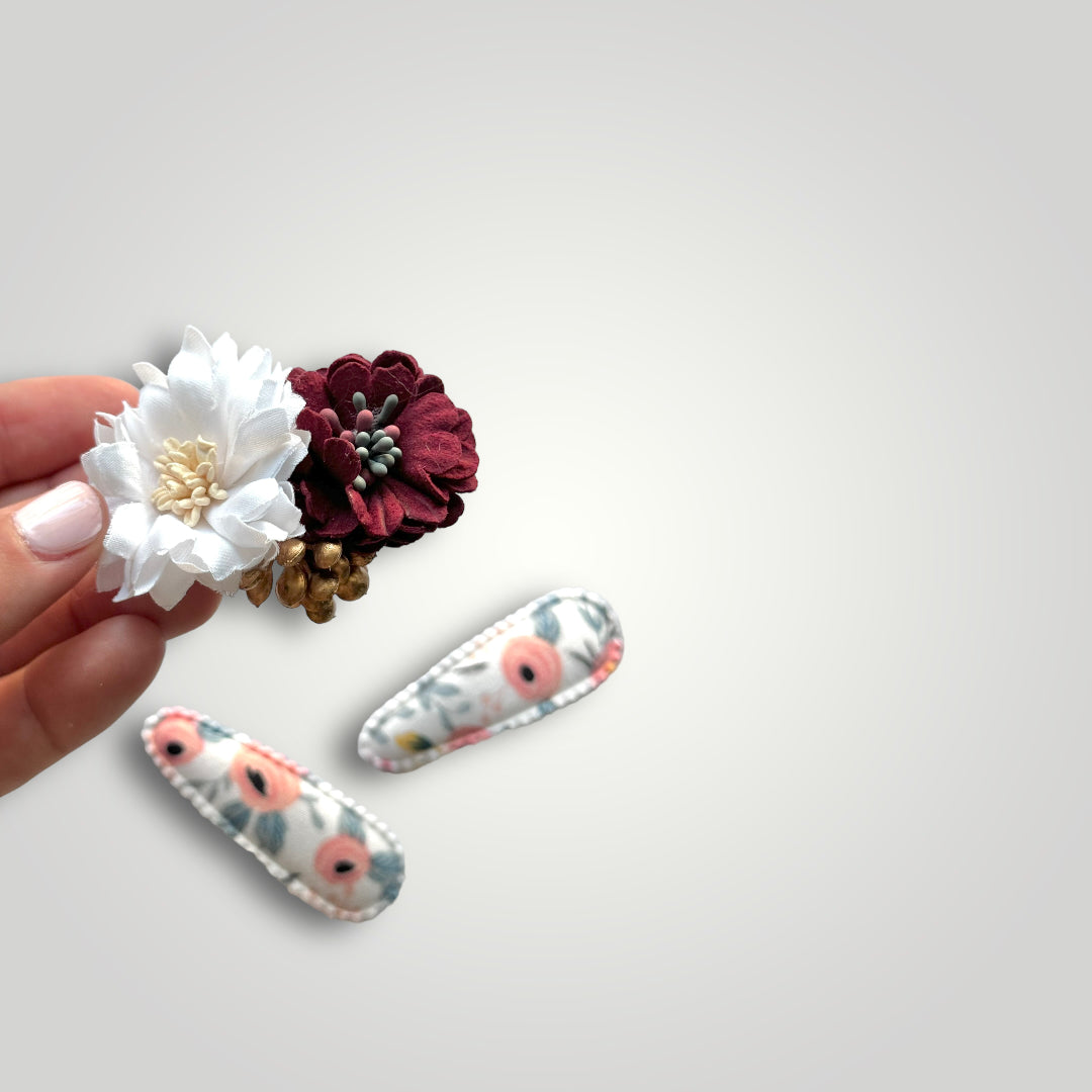 Set of 3 clips; 1 snap clip with a red and a white flower and 2 snap clips covered with fabric with flowers pattern.