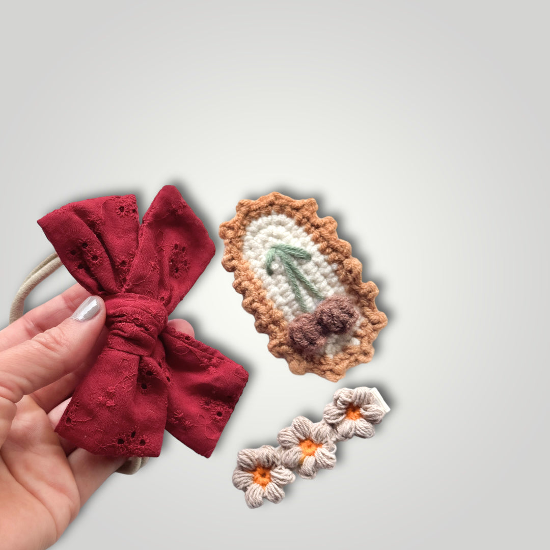 1 embroidered gauze bow in a soft headband with 2 crocheted clips, one with flowers and one with fruits. Colors: Red, brown, off white, green and orange.