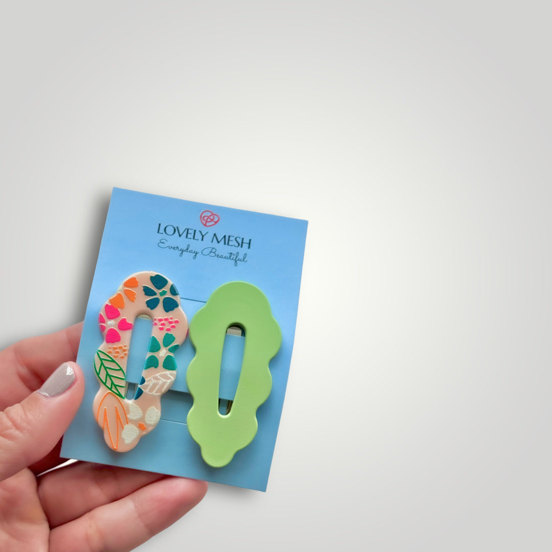 A pair of funky snap clips, colors: Green and multicolored flower pattern.