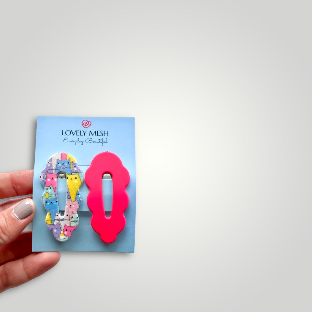 A pair of funky snap clips, colors: bright pink and multicolored cats pattern.